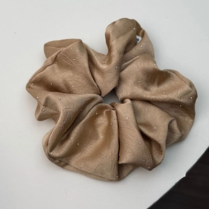 Detailed texture of champagne satin scrunchie with sparkling silver rhinestone accents
