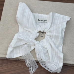 Dettaglio dello scrunchie in cotone bianco con bordo in pizzo ed etichetta su libro vintage