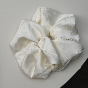 Detailed view of cream satin scrunchie with sparkling rhinestones and elegant pleated texture