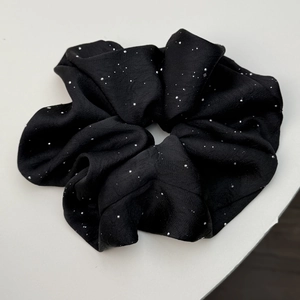Macro shot of black satin scrunchie with sparkling silver rhinestones on a white background