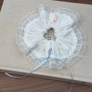 Dettaglio di scrunchie in pizzo bianco con fiocco azzurro ed etichetta cuore fatta a mano