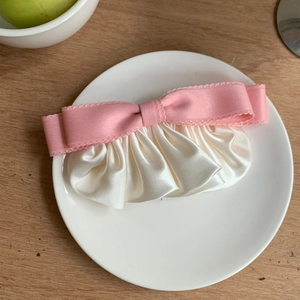 Sweet pink and white pleated satin bow hair clip with elegant ruffled edge on a plate