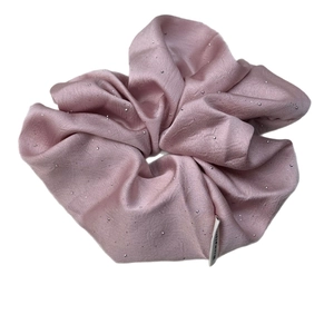 Pink satin scrunchie with sparkling rhinestones and a white brand label on a white background