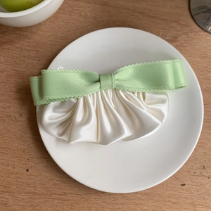Detailed view of light green ribbon bow and milky white pleated satin hair clip