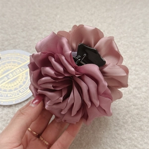 Détail d'une pince à cheveux rose poudré avec pétales satinés et poignée noire