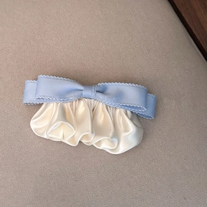 Detail of light blue silk bow hair clip with pleated cream satin fabric on beige textile