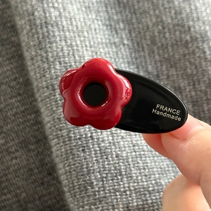 Détail d'une petite pince à cheveux fleurie avec fleur rouge et base en résine noire