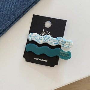 Détail de barrettes à cheveux ondulées en acétate avec logo doré sur carte noire