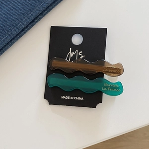 Détail de barrettes à cheveux ondulées en acétate marron et vert avec lettrage doré