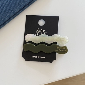 Détail de barrettes à cheveux ondulées en acétate blanc perle et vert olive sur carte