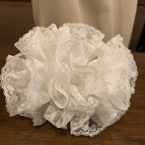 Detail of white lace hair scrunchie with layered ruffle mesh design on dark wood