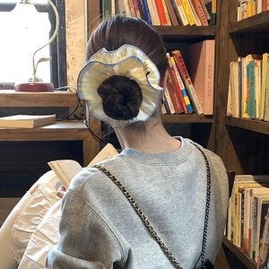 Chouchou géant à rayures jaunes et bord bleu porté sur un chignon élégant pour femme