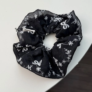 Détail d'un chouchou en résille noire avec broderie blanche et petite étiquette