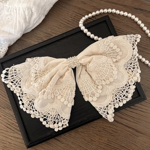 Elegant off-white lace bow hair clip with embroidered pearl accents on a wooden tray