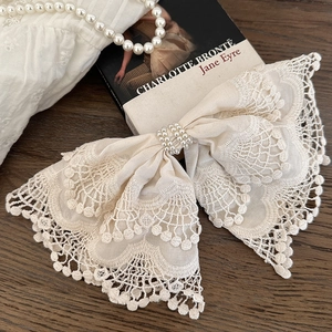 Elegant off-white lace bow hair clip with pearl embellishment on dark vintage wood