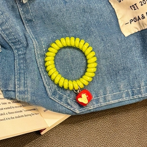 Lemon yellow telephone cord hair tie featuring a red heart apple charm on denim backdrop