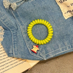 Neon green spiral telephone wire hair tie with a red apple charm on denim background