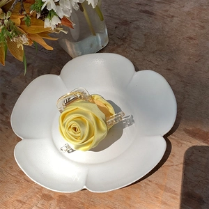 Detailed view of yellow satin handmade rose hair claw clip on white ceramic plate