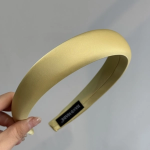 Détail du serre-tête en satin jaune montrant la texture lisse et l'étiquette faite main