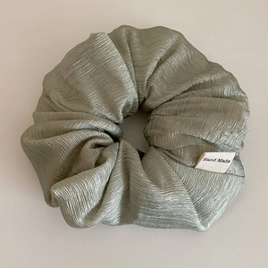 Macro shot of sage green textured silk scrunchie with a tiny Hand Made woven label