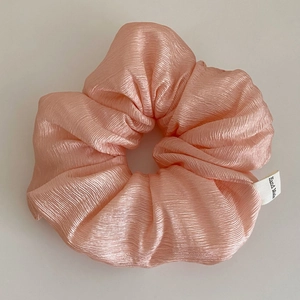 Macro shot of pink scrunchie with pleated texture and a small white handmade woven label