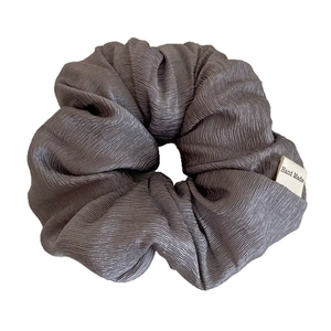 Dark grey textured scrunchie with fine pleated fabric and handmade label on white background