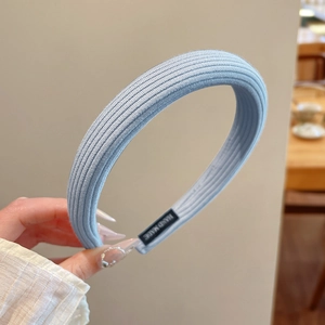 Detail of light blue pleated fabric headband with a black handmade label on inner side