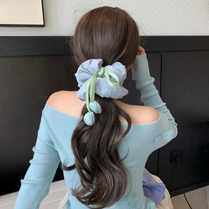 Detailed view of grey tulip scrunchie with 3D floral pendants worn on a low ponytail