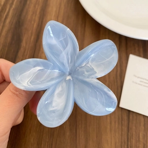 Detail showing hand holding a light blue marble-textured acetate flower hair claw clip