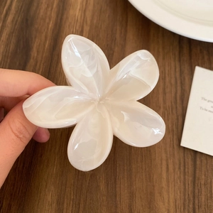 Detail of cream marbled acetate plumeria hair claw clip held by hand for size scale