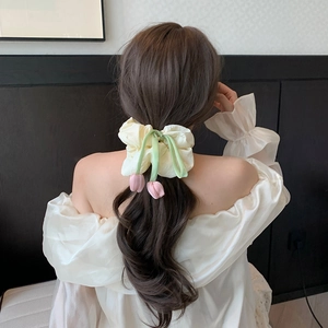 Detailed view of a cream fabric scrunchie with pink tulip pendant on dark wavy hair
