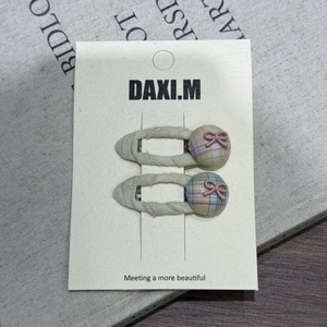 Détail de deux barrettes en tissu crème avec bouton à carreaux et nœud rose