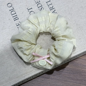 Détail d'un chouchou en tissu jaune crème avec nœud rose et bouton fait main