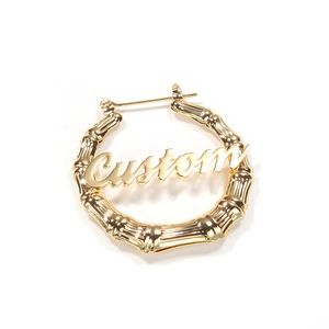 Détail de boucles d'oreilles créoles dorées avec texture bambou et motif lettre