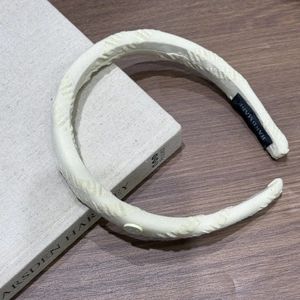 Détail d'un serre-tête rembourré crème avec texture gaufrée et étiquette faite main sur bois