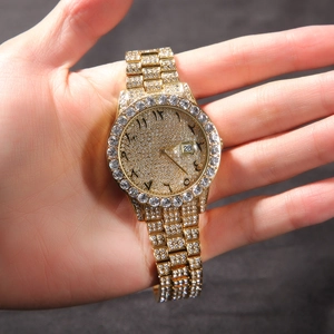 Close-up of gold iced-out watch with Arabic numerals and date window on a wrist