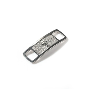Close-up of silver metal shoe lace charm featuring a zircon inlaid cross pattern