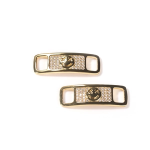 Detail of gold metal shoe lace charms with sparkling zircon cross and smile face design