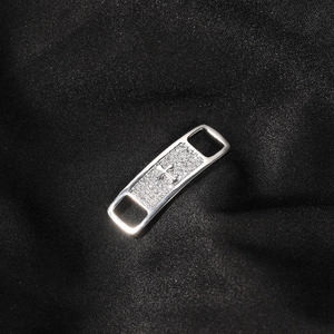 Macro shot of silver shoe buckle with zircon cross inlay on black silk fabric