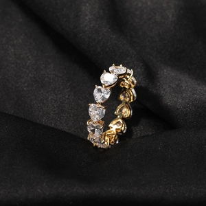 Macro shot of gold hip-hop ring with heart-cut zircons on a black silk background