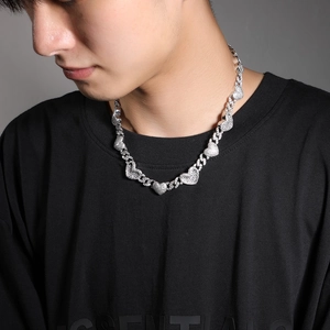Détail d'un collier chaîne cubaine argenté avec des pendentifs en cœur sur un mannequin