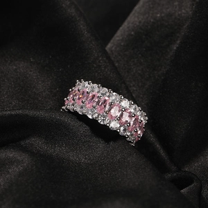 Nahaufnahme von rosa ovalem Zirkonia und weißen Steinen auf einem Silberring auf Seide