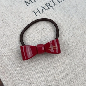 Detail of red acetate bow hair tie with gold France Handmade logo and elastic band
