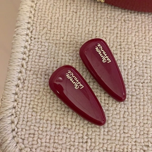 Close-up of wine red drop-shaped hair clips with gold lettering on knit fabric