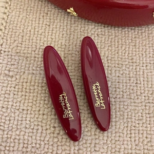 Detail of dark red oval hair clips with gold Barrette Lafrance script on beige fabric