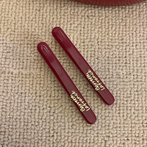Detail view of two dark red resin hair clips with golden French script on knit fabric