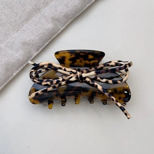 Detail of tortoiseshell hair claw clip with leopard print bow on a minimal background