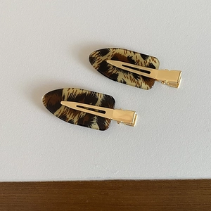 Detail view of two seamless leopard print oval hair clips with gold metal base