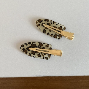Close-up of two leopard print hair clips with golden metal clips on a grey desk