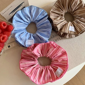 Close-up of three striped fabric scrunchies in blue, brown, and pink with ribbon labels